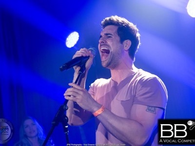 Male vocalist performing on stage with microphone under blue concert lighting and spotlights, demonstrating professional stage lighting setup.