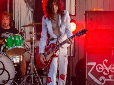 Guitarist performs on stage with red lighting and drum kit visible, showcasing professional concert audio and lighting setup at Fox Lake Venetian Night 2025.